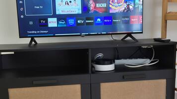 Musta, litteä näyttöinen televisio on sijoitettu mustalle viihdekeskukselle, ja sen edessä on puinen pöytä.