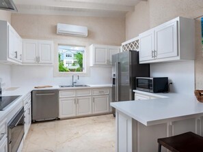 Cozinha moderna com armários brancos, eletrodomésticos de aço inoxidável e janela com vista para o verde lá fora.