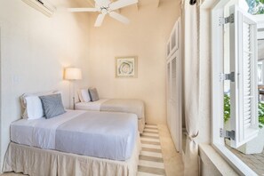 Quarto com duas camas, um ventilador de teto, abajur e janela com persianas.