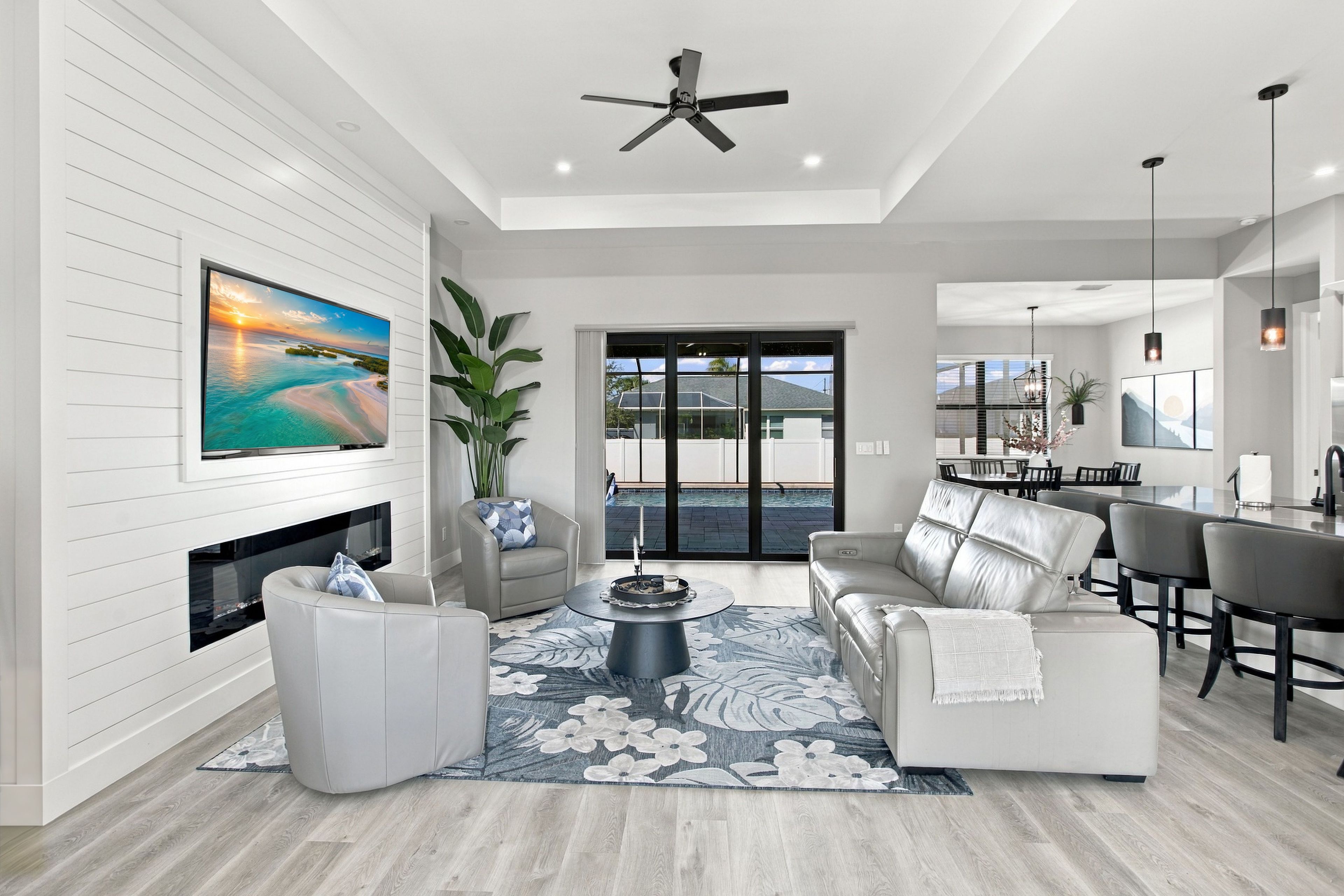 A modern living room with a fireplace, a large flat-screen TV, a ceiling fan, and a dining area with a bar.