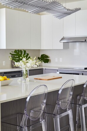 Une cuisine moderne avec des meubles blancs, un îlot central dot é de tabourets de bar, un vase rempli de fleurs et une planche à découper en bois.