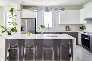 A modern kitchen with a central island, stainless steel appliances, and clear plastic bar stools. - Live Life-3BR Luxury Oceanfront Condo in Freeport (Montego Bay)