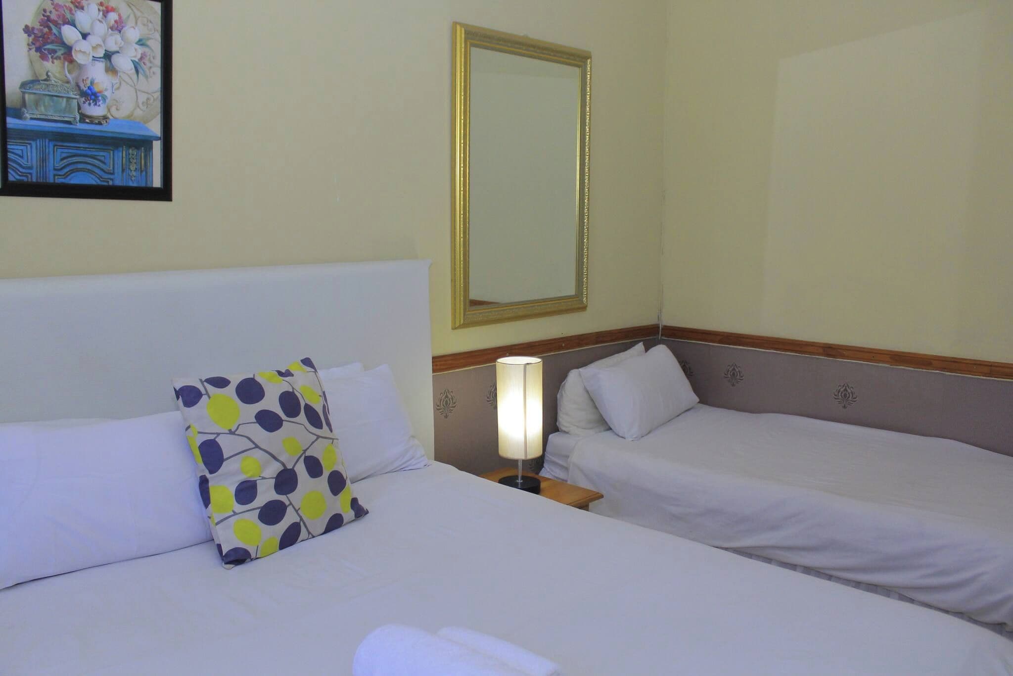 Habitación de hotel con dos camas, una mesita de noche, una lámpara y un espejo en la pared.