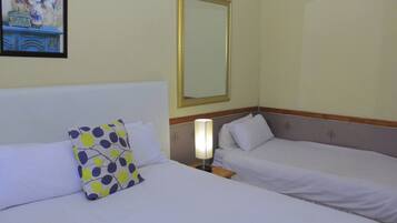 Habitación de hotel con dos camas, una mesita de noche, una lámpara y un espejo en la pared.