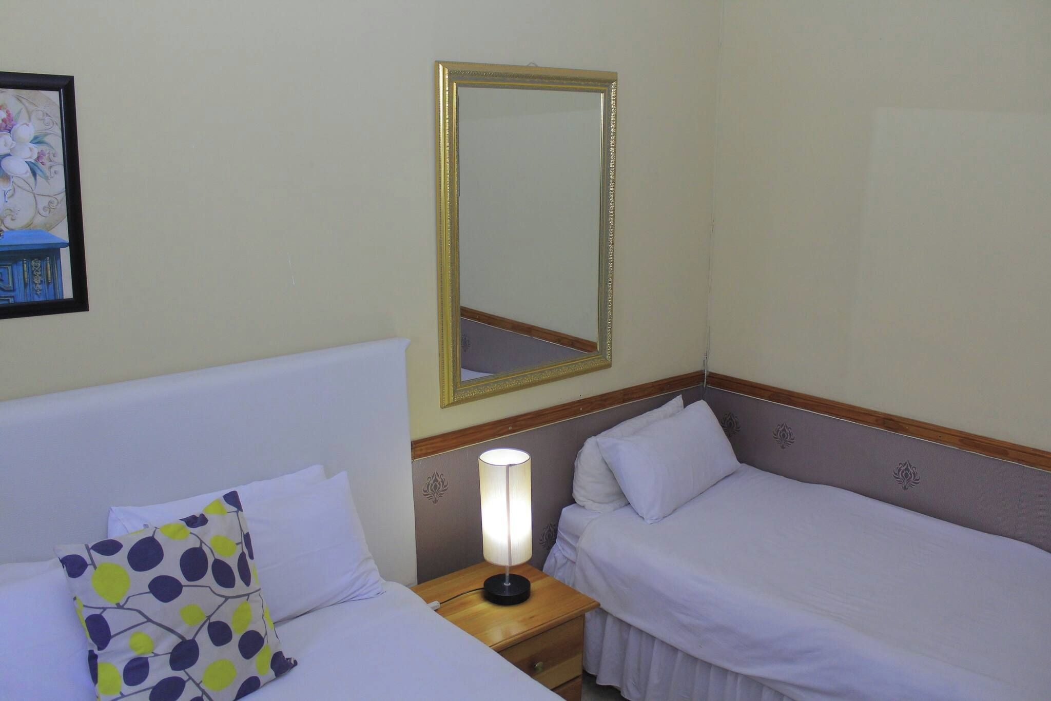 A hotel room with a bed, a bedside lamp, a mirror, and a wall decoration.