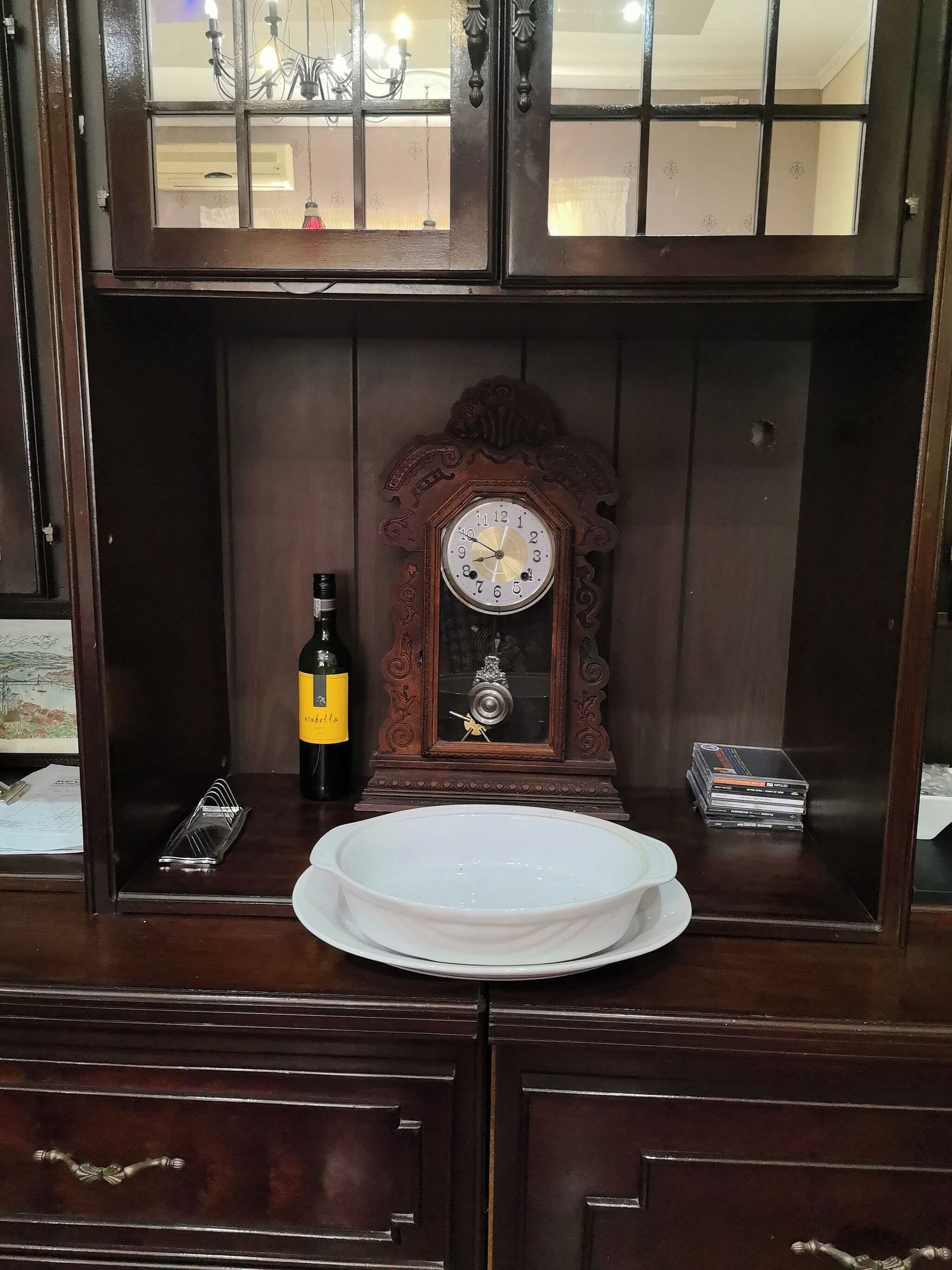 Un mueble de madera con un reloj, una botella y una pila de DVD.