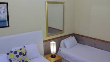 A hotel room with two single beds, a nightstand with a lamp, and a mirror on the wall.