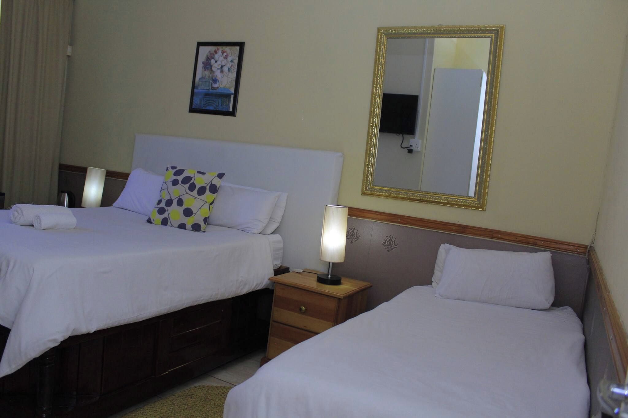 A hotel room with two beds, a nightstand, a lamp, a mirror, and a painting on the wall.
