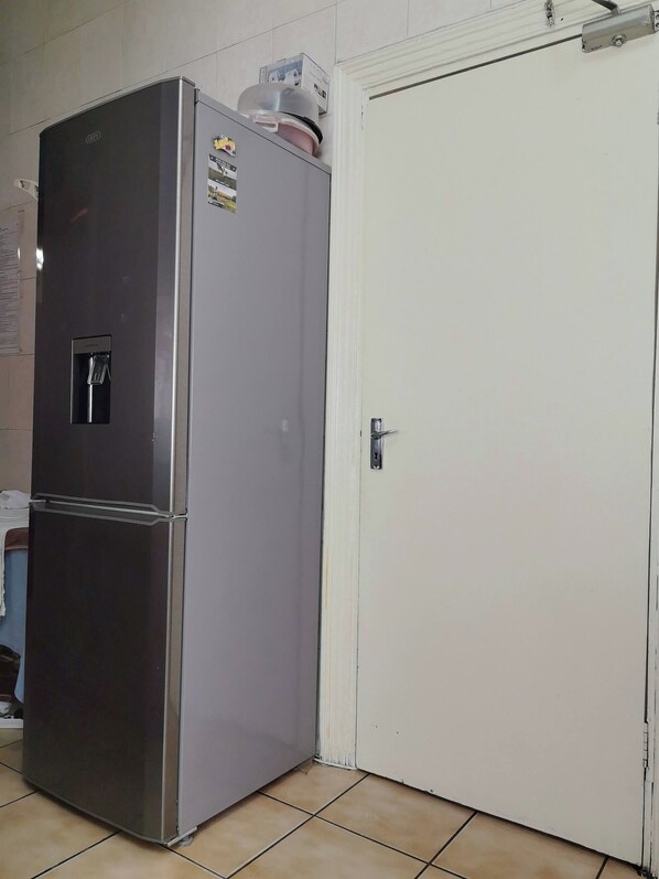 Un refrigerador de acero inoxidable con dispensador de agua, puerta blanca y piso de baldosas.