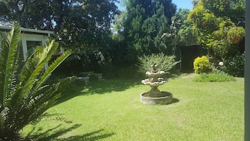 Een verzorgde tuin met een fontein in het midden, omringd door weelderig groen en diverse bomen.