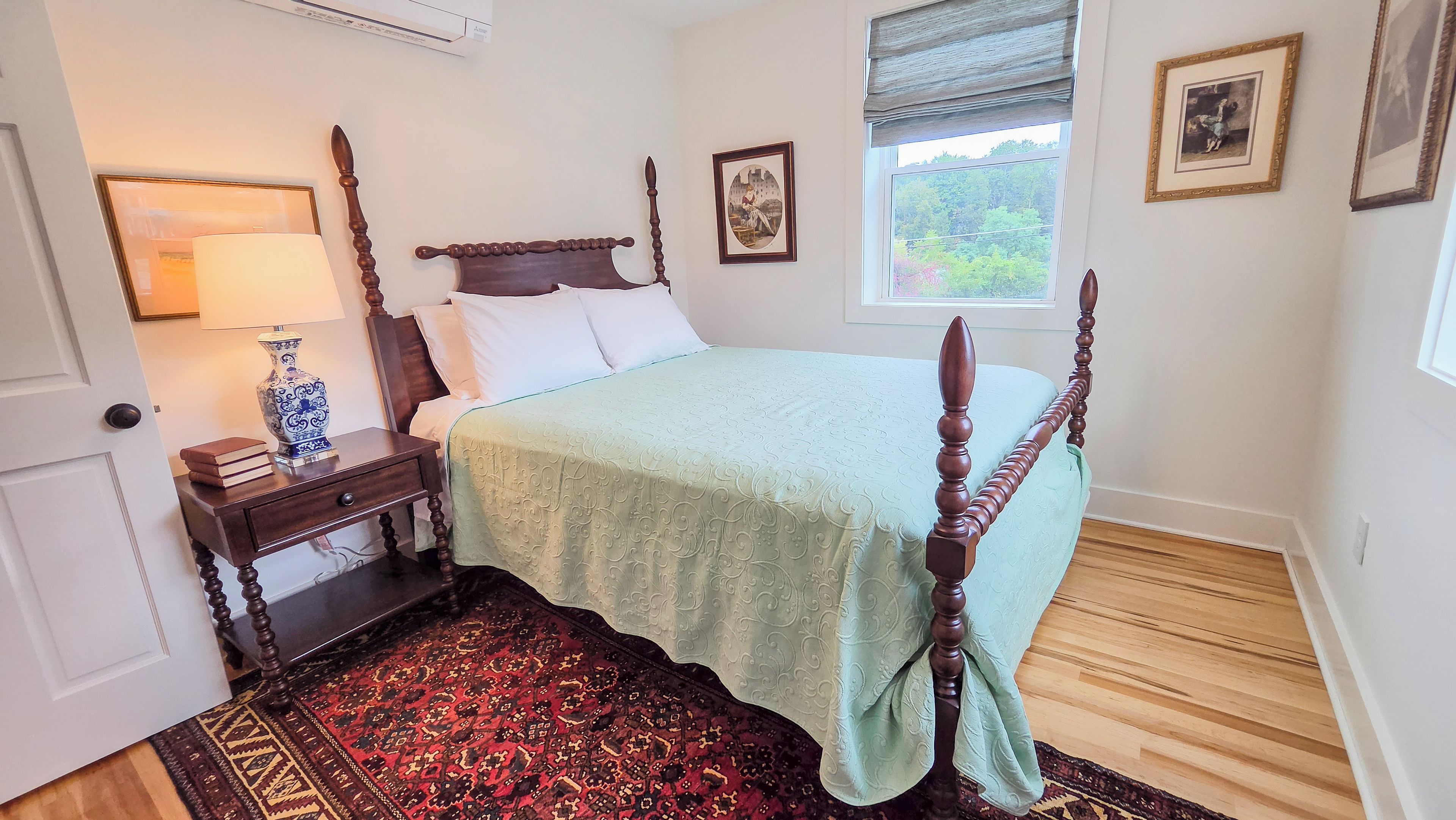 Une chambre à coucher avec un lit à baldaquin, une table de chevet avec une lampe, un tapis et des tableaux encadrés accrochés au mur.