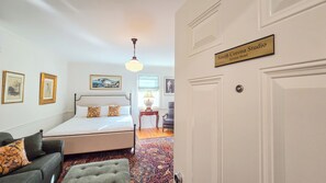 A hotel room with a bed, a chair, a lamp, and a door labeled 'Smith Corona Studio Groton Hotel'.