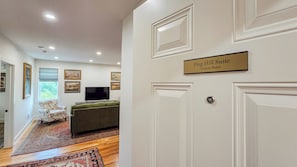 A hotel suite with a flat-screen TV, a sofa, and a dining table. There are framed pictures on the wall and a window with a view.
