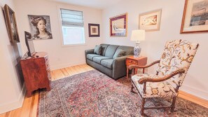 A living room with a grey sofa, a patterned armchair, a wooden cabinet, and a rug.