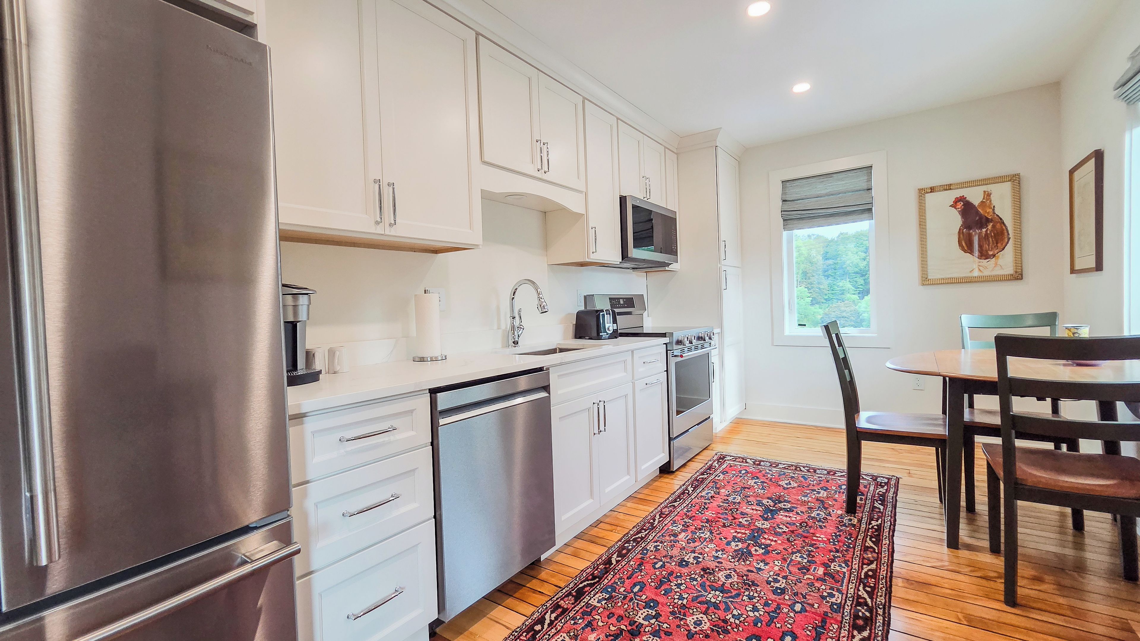 A modern kitchen with stainless steel appliances, white cabinetry, and a dining area with a wooden table and chairs.