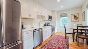 A modern kitchen with stainless steel appliances, white cabinetry, and a dining area with a wooden table and chairs.