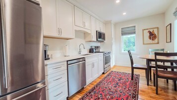 Una cocina moderna con electrodomésticos de acero inoxidable, armarios blancos y un comedor con mesa y sillas de madera.