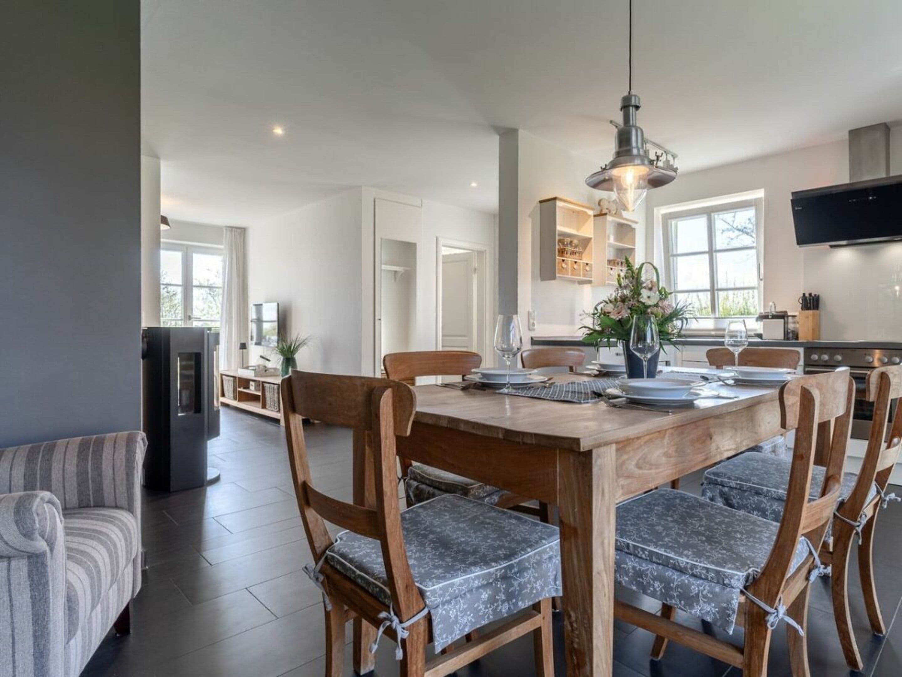 A modern dining area with a wooden table and chairs, a pendant light, and a kitchen in the background.