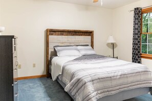 Une chambre à coucher avec un lit, une table de chevet, une lampe et une fenêtre avec des rideaux.