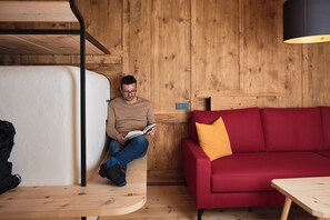 A person sitting on a bench reading a book in a room with wooden walls, a red sofa, and a wooden table.