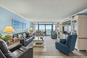 A spacious living room with a sofa, armchairs, and a coffee table. There is a balcony with a view of the sea. - 2BR/2BA Oceanfront- Pool- Brigadune I 11D (Myrtle Beach)