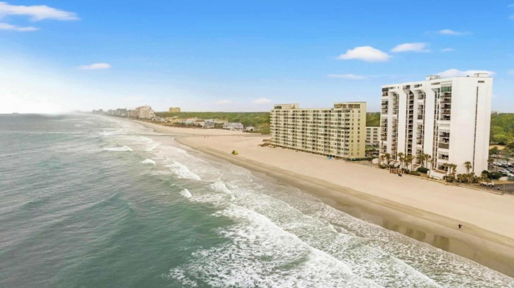 A beachfront hotel with multiple buildings, a sandy beach, and the ocean.