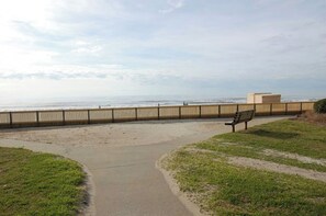 Ein Küstenwanderweg mit Holzzaun, Bank und freiem Blick auf das Meer.