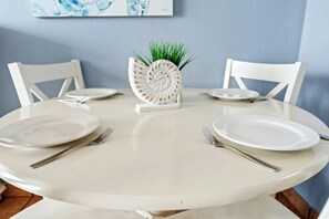 A round dining table with white plates, silver cutlery, and a decorative white centerpiece. - Bay Watch 735- Oceanfront 1BR- Pools (North Myrtle Beach)
