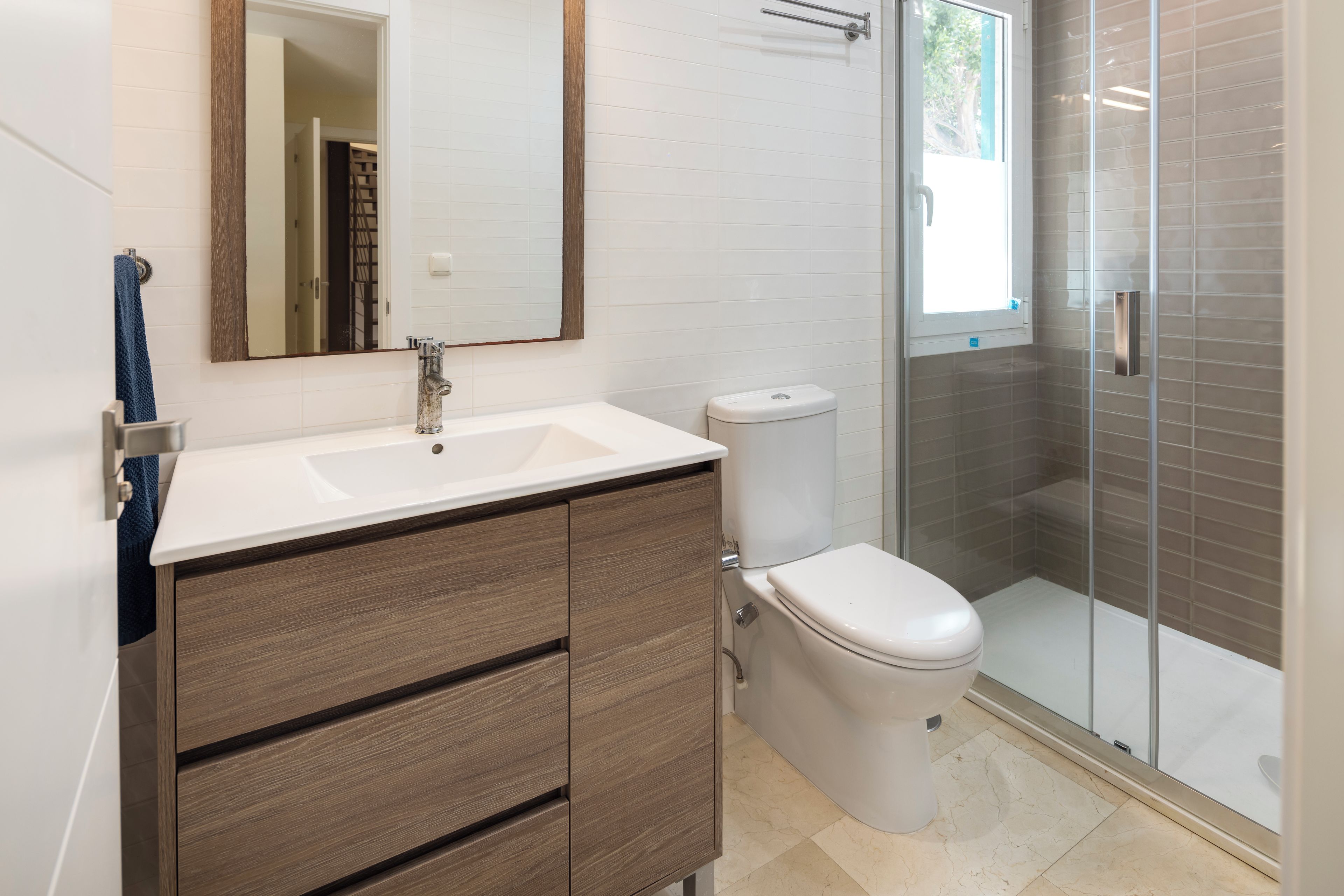 Een moderne badkamer met een wit wastafel, houten wastafelmeubel, toilet en een douchecabine met glazen wanden.