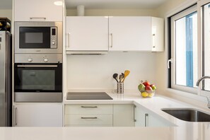 A modern kitchen with stainless steel appliances, white cabinetry, a fruit bowl, and a window with a view.