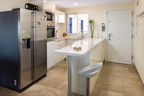 A modern kitchen with a stainless steel refrigerator, a microwave, and an oven. There is a white countertop with a sink and a vase with candles. - Fabulous 4-Bedroom Beachfront Townhouse in Málaga (Málaga)
