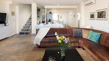 Een moderne woonkamer met een bruine leren bank, een salontafel met een bloevas, en een flatscreen televisie die aan de muur is bevestigd.