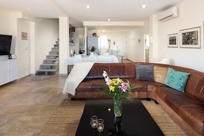 A modern living room with a brown leather sofa, a coffee table with a vase of flowers, and a flat-screen TV mounted on the wall.