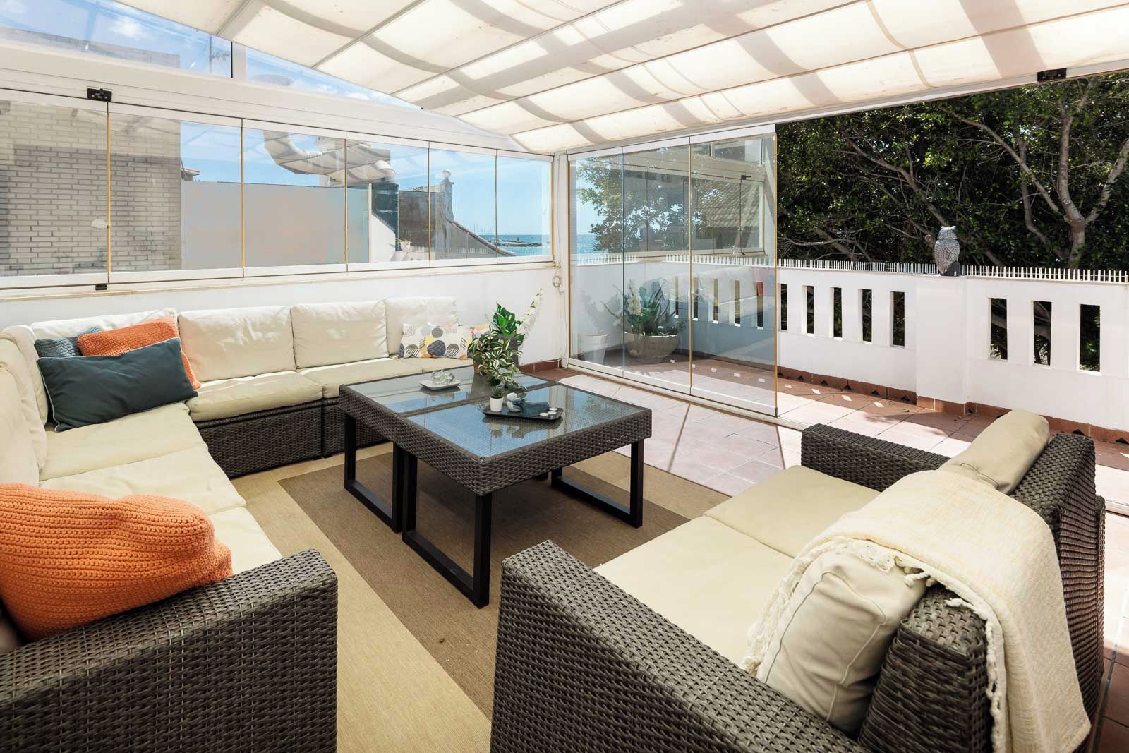 Un patio soleado con muebles de mimbre, una mesa de cristal y vista al mar.