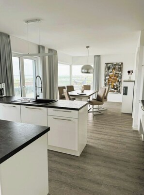 A modern kitchen with a central island, dining area with chairs, and a large window providing a view. - Holiday Apartment With 2 Bedrooms (Wangerland)