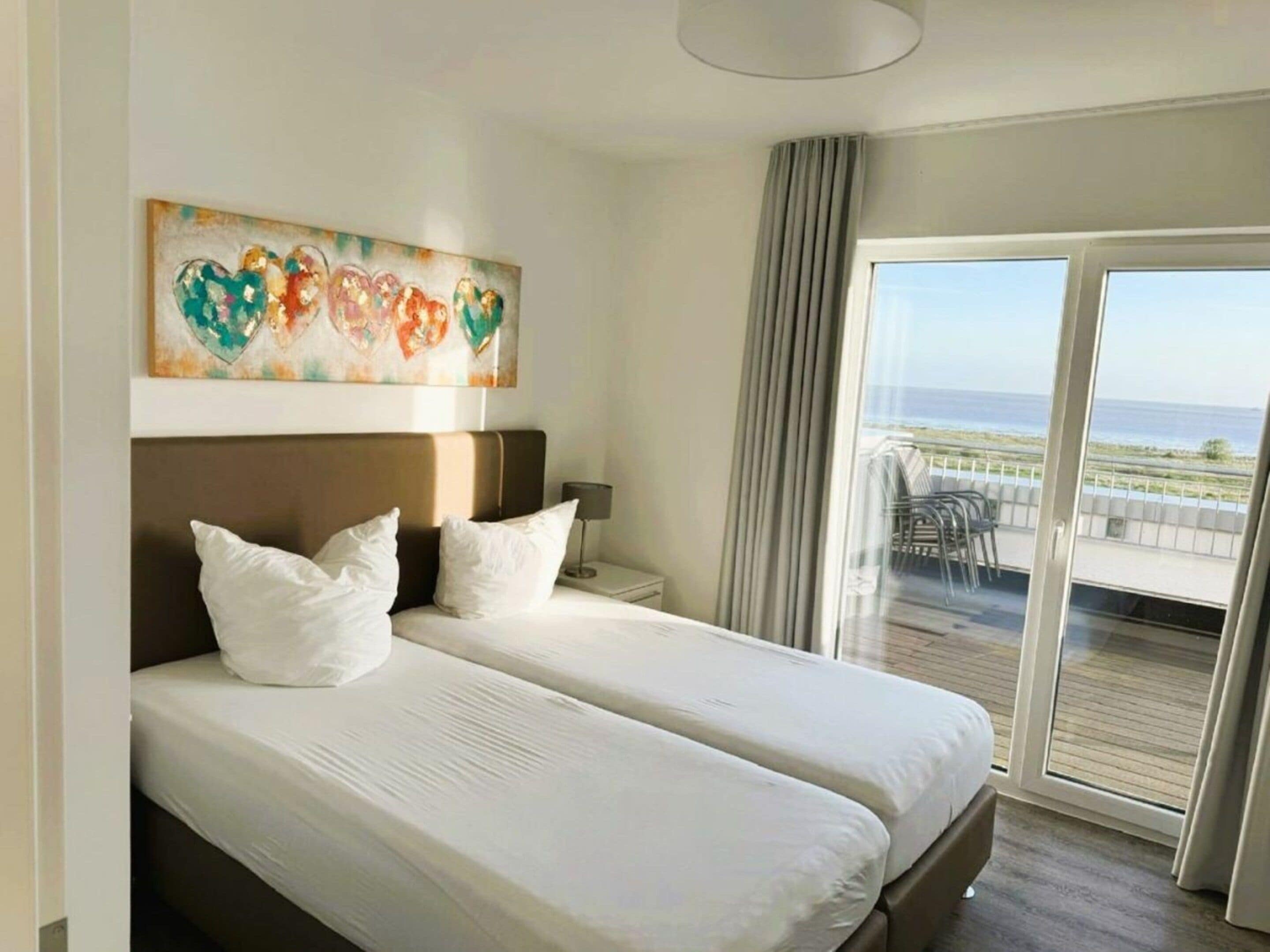 Une chambre d’hôtel avec un lit, un tableau, une table de chevet et une vue sur la mer, visible à travers une porte coulissante.
