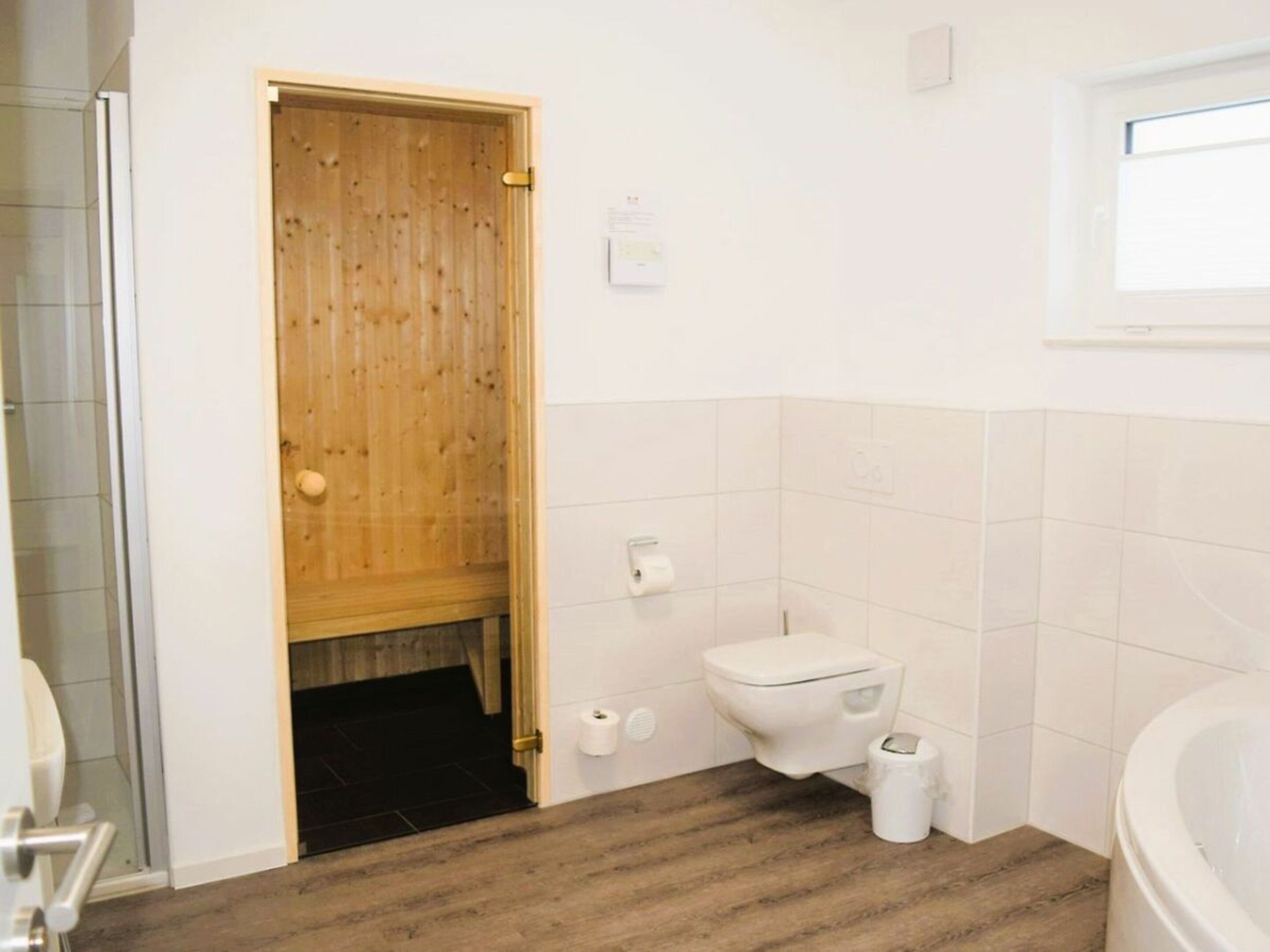 A bathroom with a wooden door, a toilet, a bidet, and a bathtub.