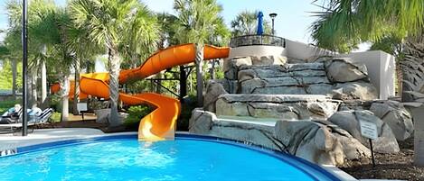 Una piscina con tobogán y una estructura rocosa.