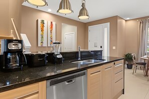 Eine moderne Küche mit Geschirrspüler, Kaffeemaschine und Mixer. Zwei weiße Türen und ein Fenster mit Vorhängen.