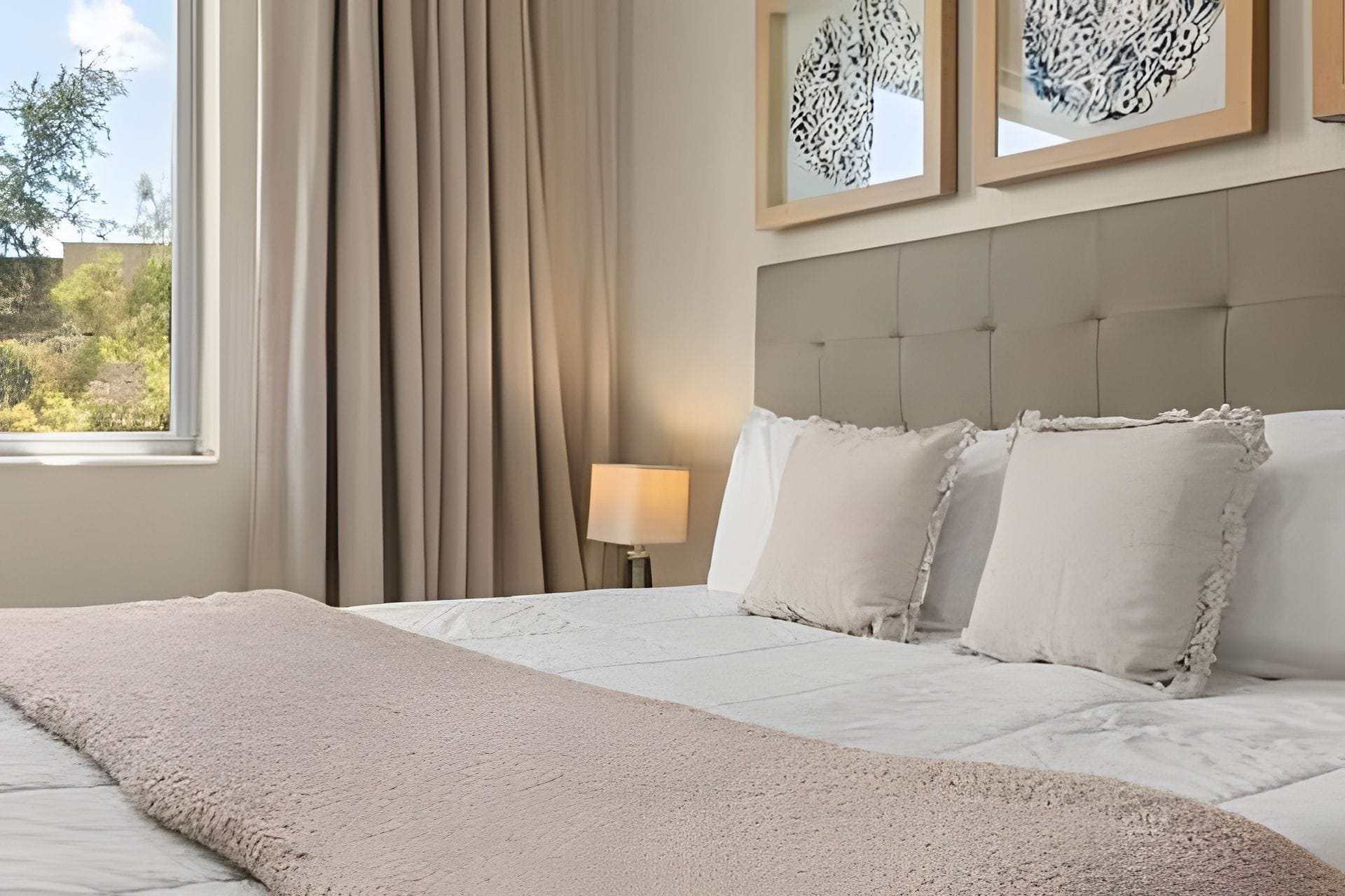 A hotel room with a bed, curtains, a lamp, and framed artwork on the wall.