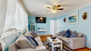 A living room with two sofas, a coffee table, a ceiling fan, a TV, and a painting on the wall. - The Ocean Rancher - 40 Woodland Ave (Ocean View)