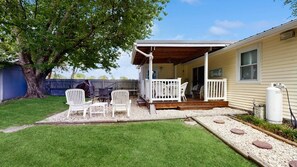 A covered outdoor seating area with white chairs and a wooden deck, a large tree, and a house with a 'Beach' sign. - The Ocean Rancher - 40 Woodland Ave (Ocean View)