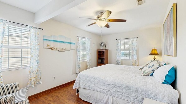 A bedroom with a bed, a ceiling fan, a window with curtains, a bedside table, and a lamp. - The Ocean Rancher - 40 Woodland Ave (Ocean View)