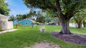 A backyard with a swing set, a tree, and a blue house. - The Ocean Rancher - 40 Woodland Ave (Ocean View)