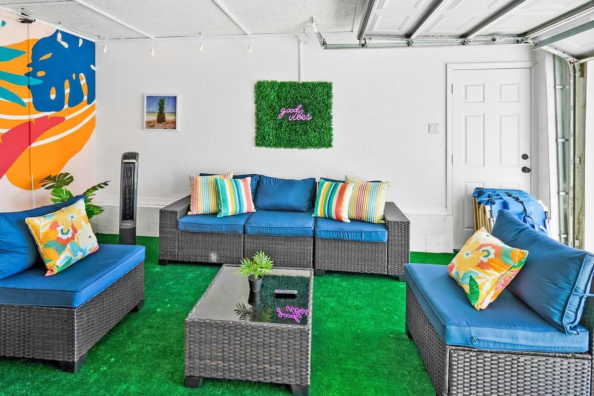 Un salon accueillant, avec des meubles en osier, un sol recouvert d’un gazon synthétique vert et une décoration murale aux motifs positifs.