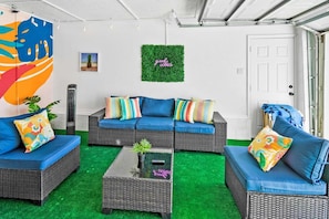 Un salon accueillant, avec des meubles en osier, un sol recouvert d’un gazon synthétique vert et une décoration murale aux motifs positifs.