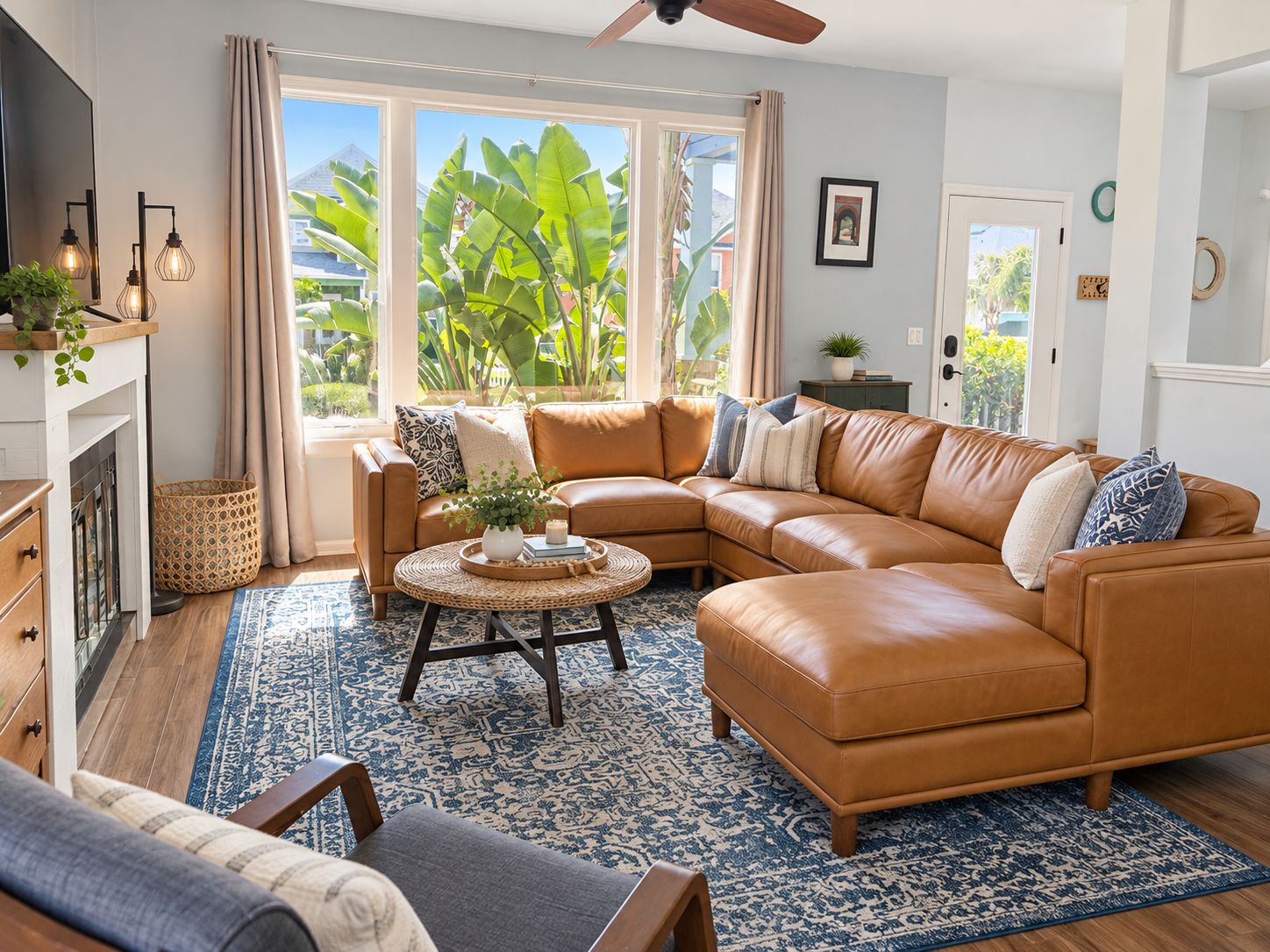 A living room with a brown leather sectional sofa, a round coffee table, a patterned rug, and a large window with a view of greenery.