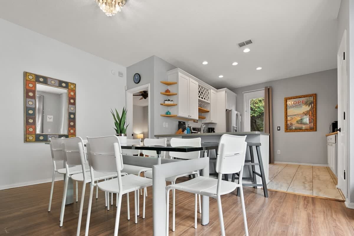 Une cuisine moderne avec des meubles blancs, un coin repas avec des chaises blanches et un plancher en bois.