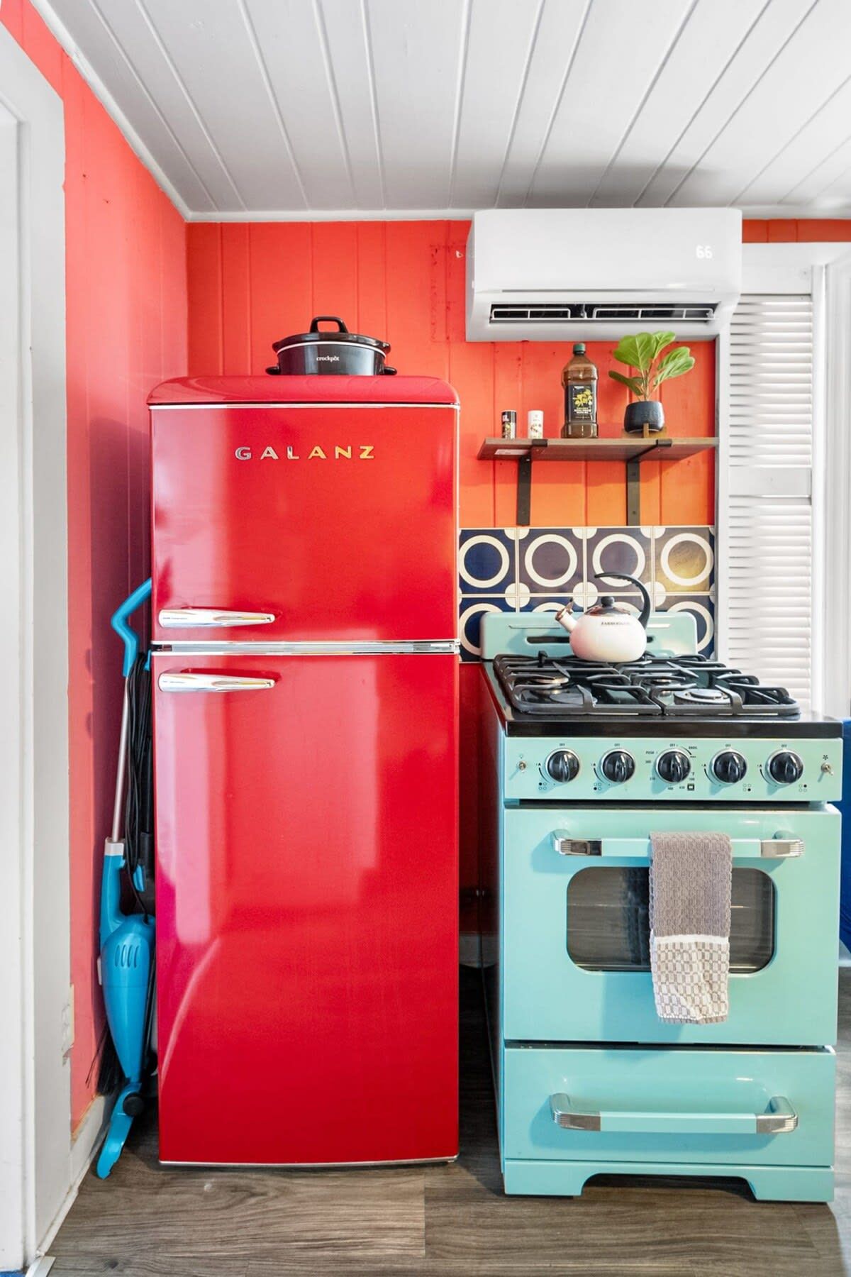 Une cuisine avec un réfrigérateur rouge, une cuisinière bleue et un plafond blanc.