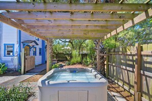 A hot tub under a wooden pergola in a backyard with a blue house and a wooden fence. - Sleeps 3 · Pet Friendly · Shared Hot Tub (Saint Augustine)